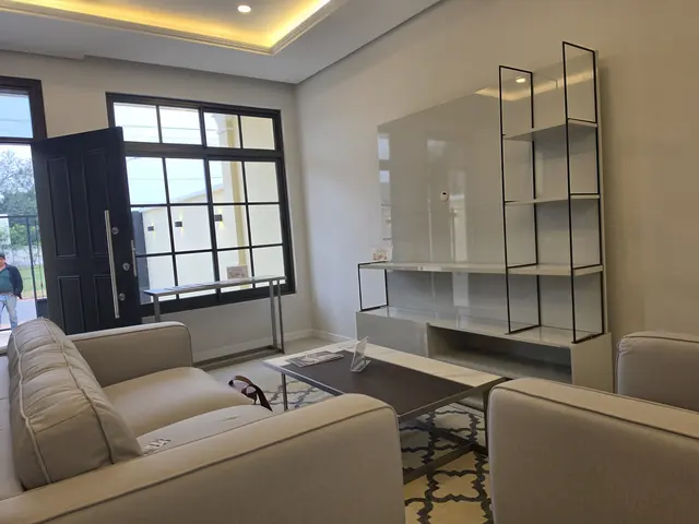 Sala de estar de la casa modelo, con ventanales de marco negro y mueble de televisión